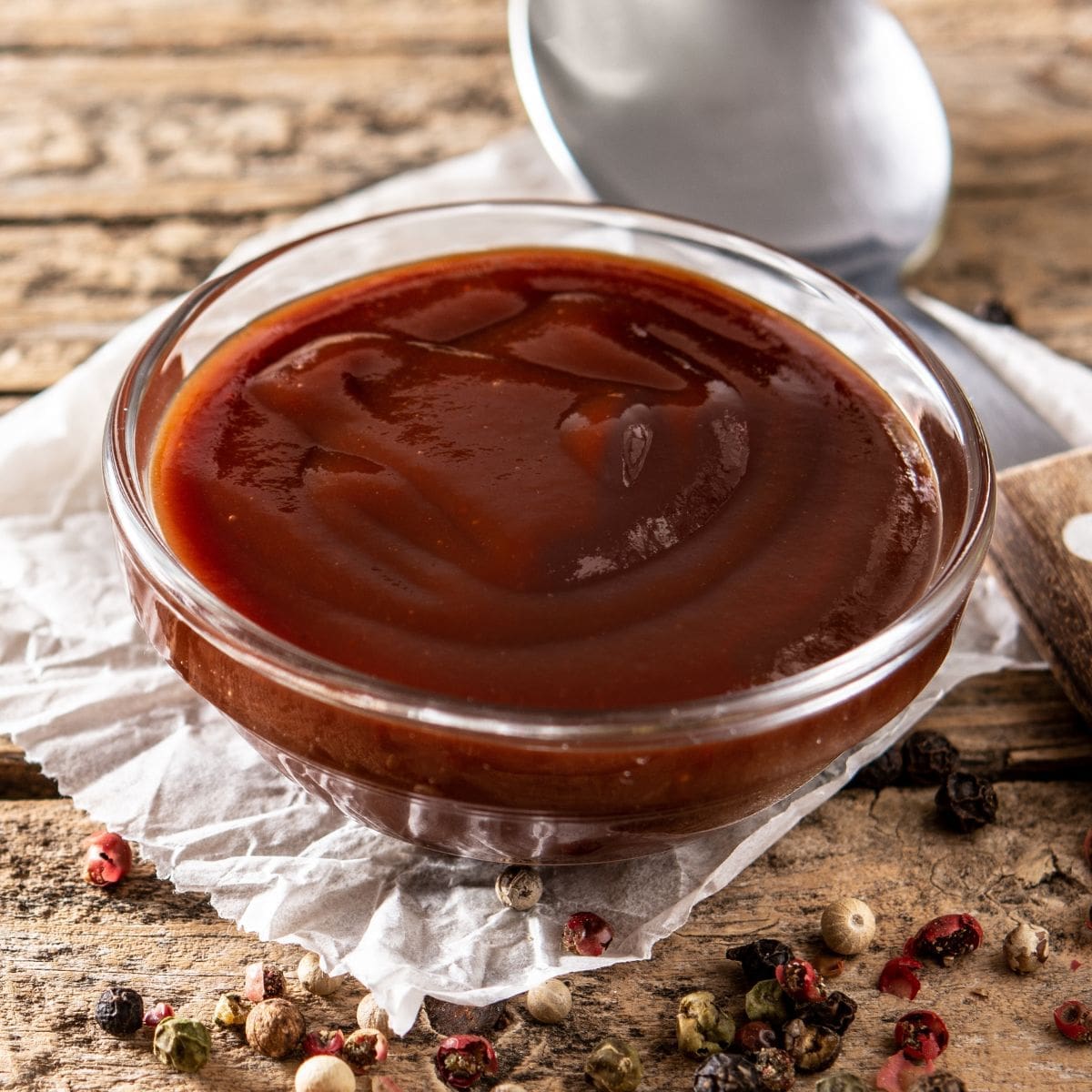 A close-up photo of a rustic wooden table with a small bowl of dark red barbecue sauce.