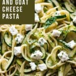 close-up photo of a rustic red ceramic bowl containing a serving of fettuccine pasta with long ribbons of zucchini and crumbled goat cheese.
