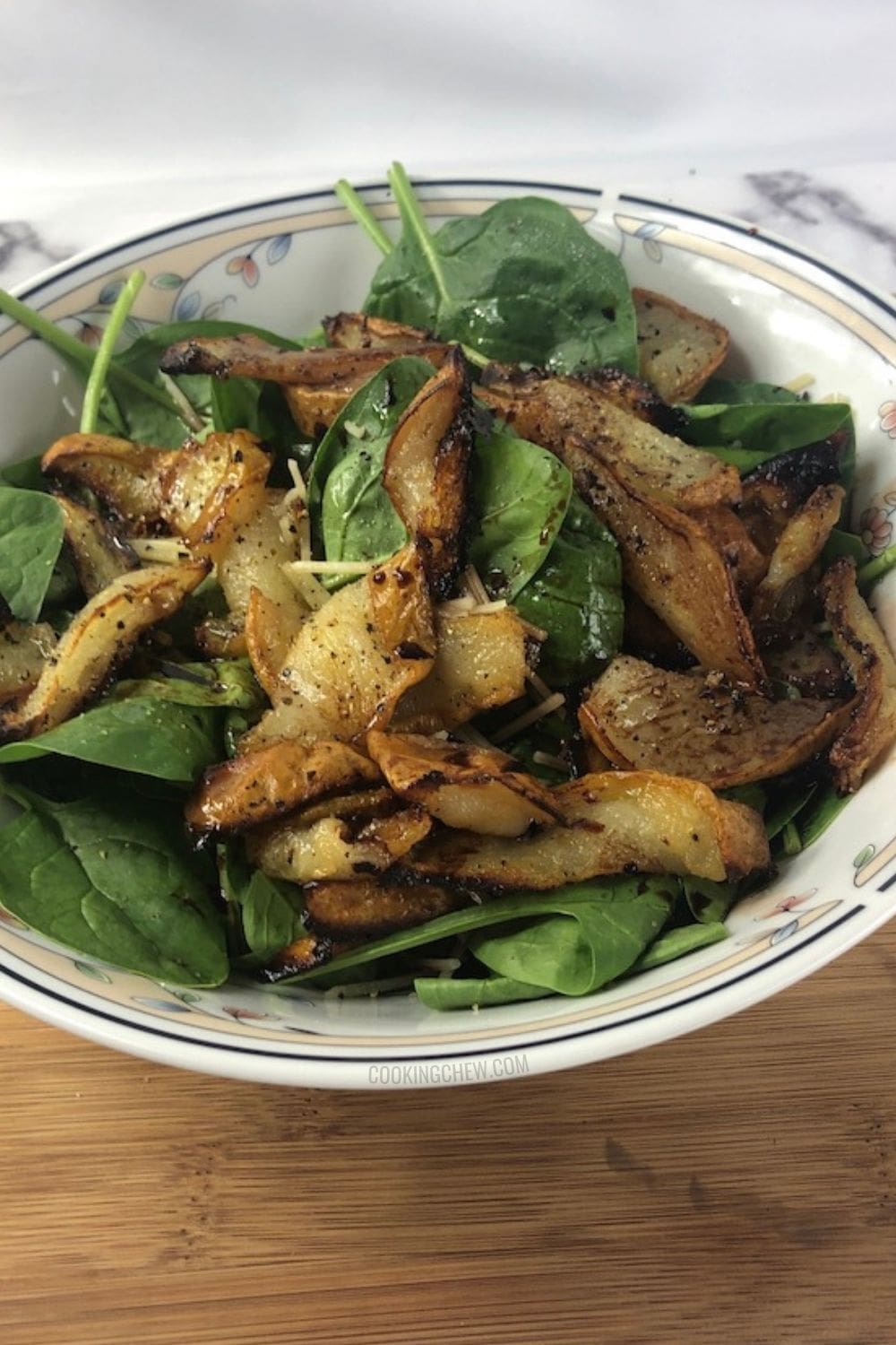 A close-up photo of a bowl of spinach salad with roasted pear with balsamic reduction on a wooden cutting board.