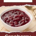 The image shows a bowl of cranberry pear sauce with a spoon on a wooden table.