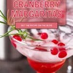 A glass of Tangy Cranberry Margarita on a wooden table. The margarita has a deep red color and is garnished with fresh cranberries and a rosemary sprig.