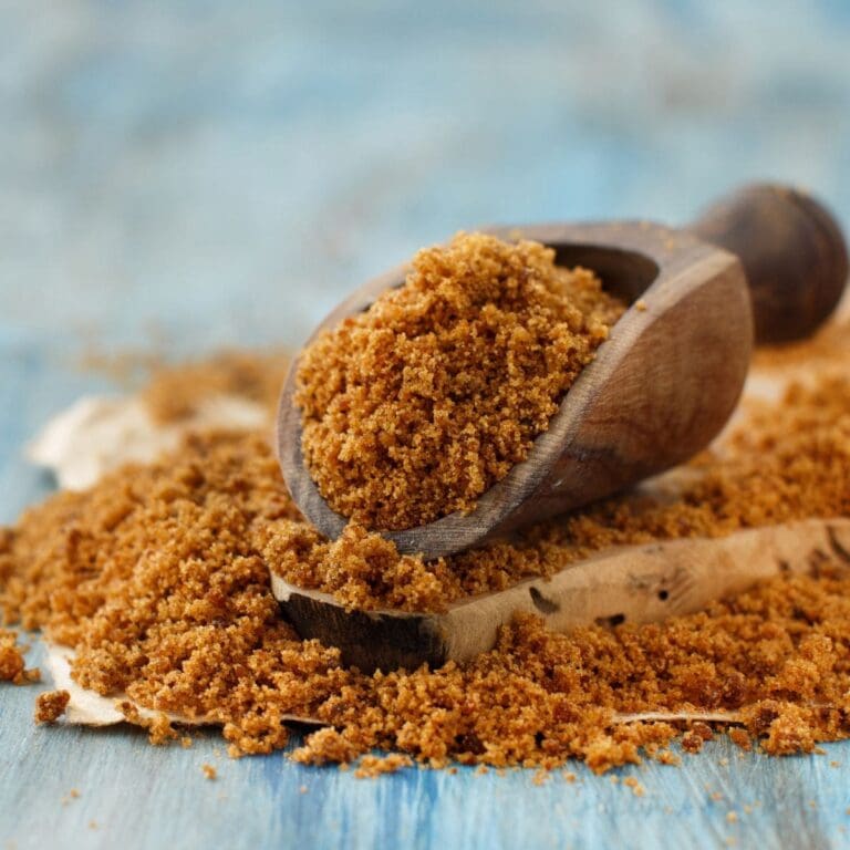 A wooden scoop filled with brown sugar is resting on a wooden table.