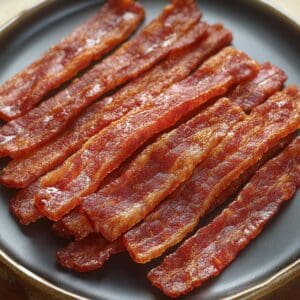 A close-up of turkey bacon frying in a pan, sizzling with crispy edges.