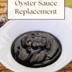 A close-up photo of a bowl of oyster sauce, an oyster shell, and a lime on a wooden table.