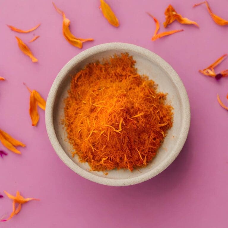 A bowl of saffron powder and threads on a pink background.