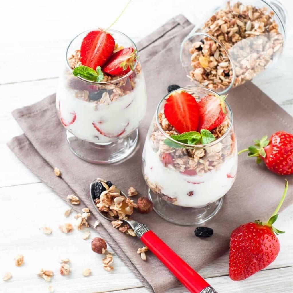 Two glasses of yogurt and granola parfaits layered with fresh strawberries.