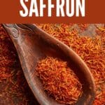 A wooden spoon filled with saffron threads on a wooden table.