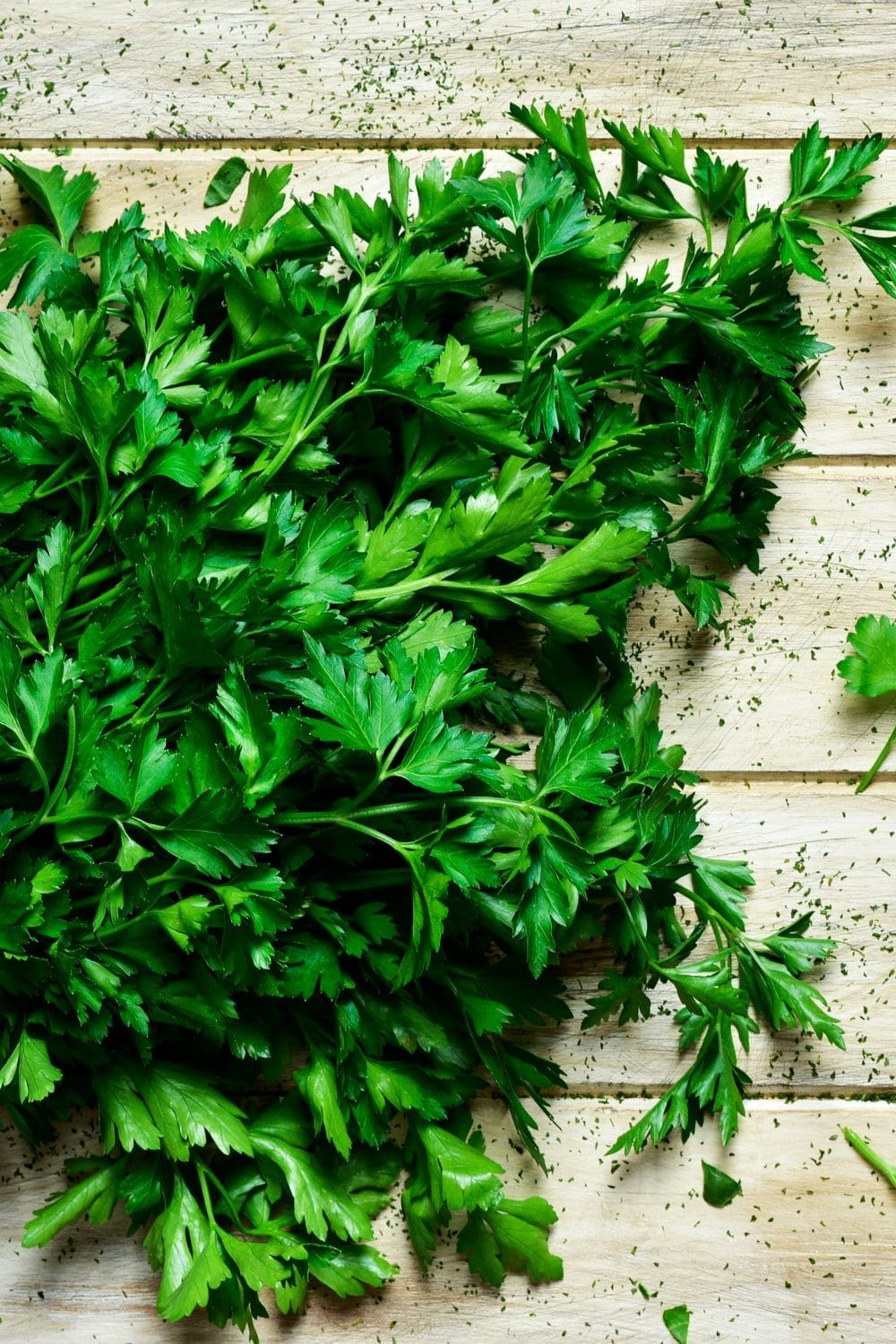 The image shows a bunch of parsley leaves on a wooden table.