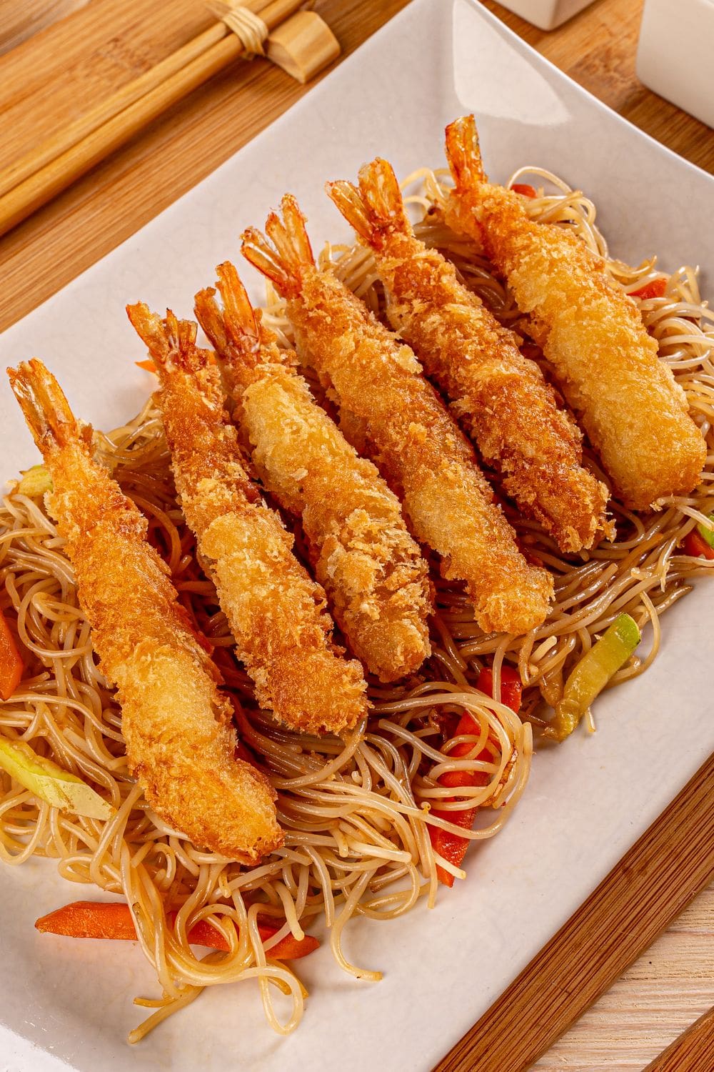A photo of a plate of air fried breaded shrimp, udon noodles, and vegetables.