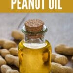 A transparent bottle of peanut oil around a pile of peanuts