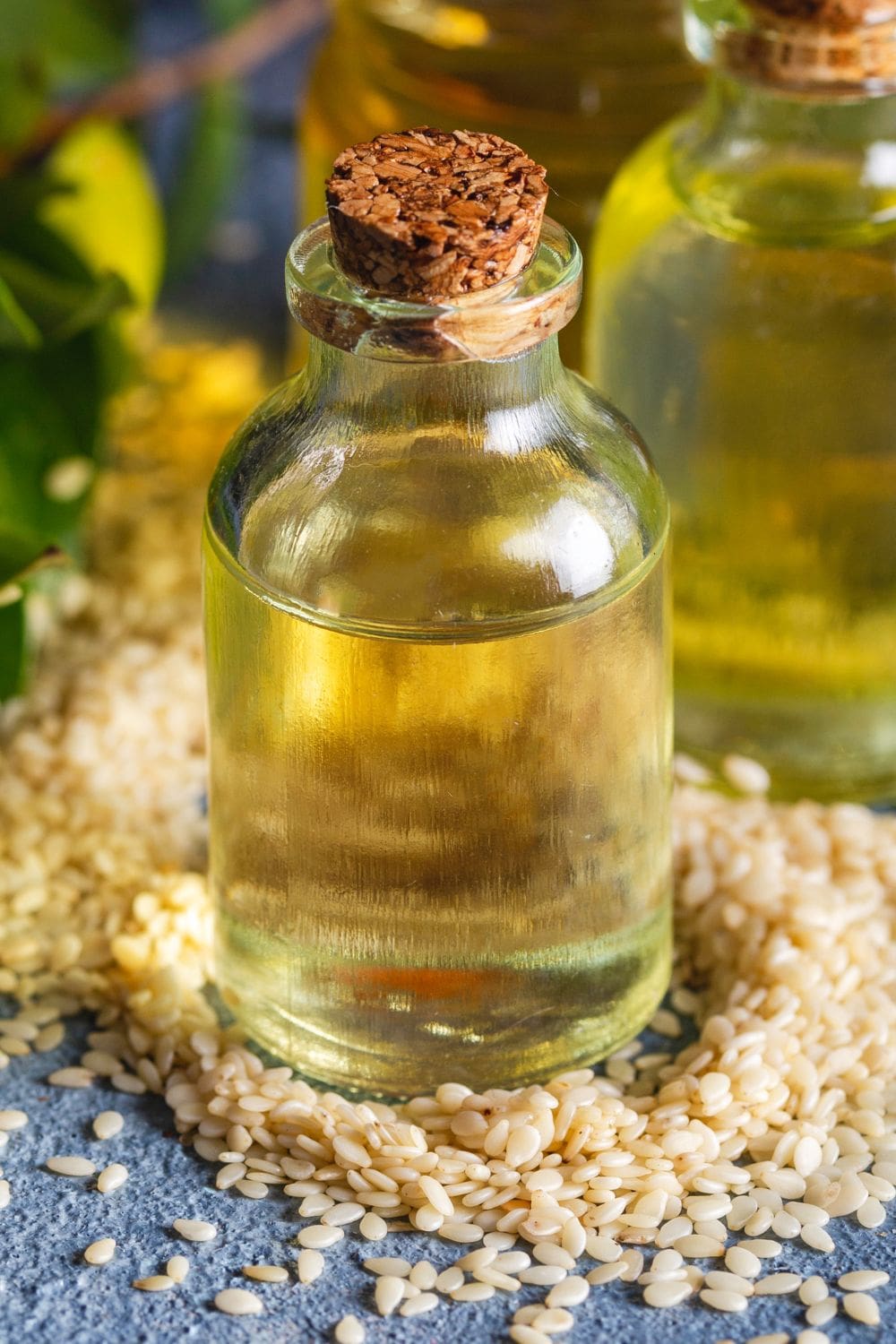 A bottle of sesame oil and sesame seeds sit on a wooden table.