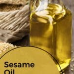 A bottle of sesame oil next to a basket of sesame seeds on a wooden table.