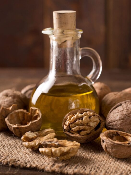 A bottle of walnut oil surrounded by walnuts on a table.