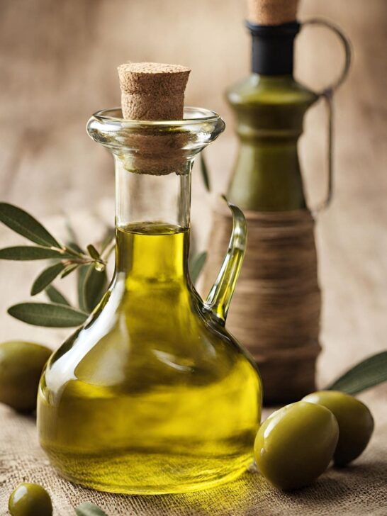Two bottles of olive oil and green olives on a wooden table.