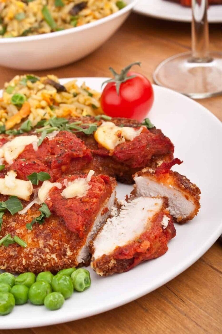A close-up photo of a sliced chicken parmesan dinner on a white plate.