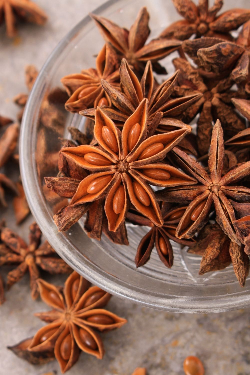 A close-up photo of a glass bowl filled with whole star anise pods on a light wooden table. 