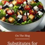 A bowl of mixed greens with cherry tomatoes, cucumbers, red onions, and a light balsamic vinegar being drizzled on top from a silver spoon.