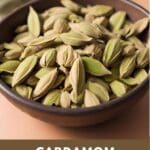 A close-up photo of a small, round wooden bowl filled with cardamom pods