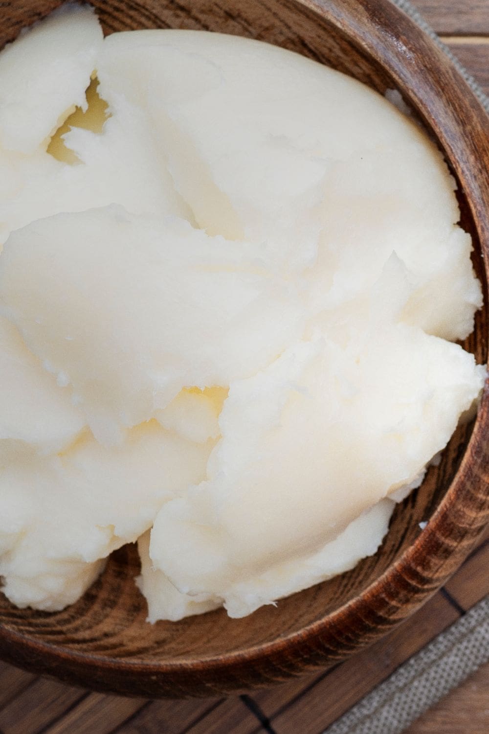A close-up photo of a round, wooden bowl filled with white lard. 