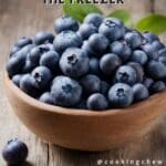 A close-up photo of a small wooden bowl filled with fresh blueberries.
