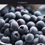 A pile of frozen blueberries on a wooden table, next to a metal spoon.