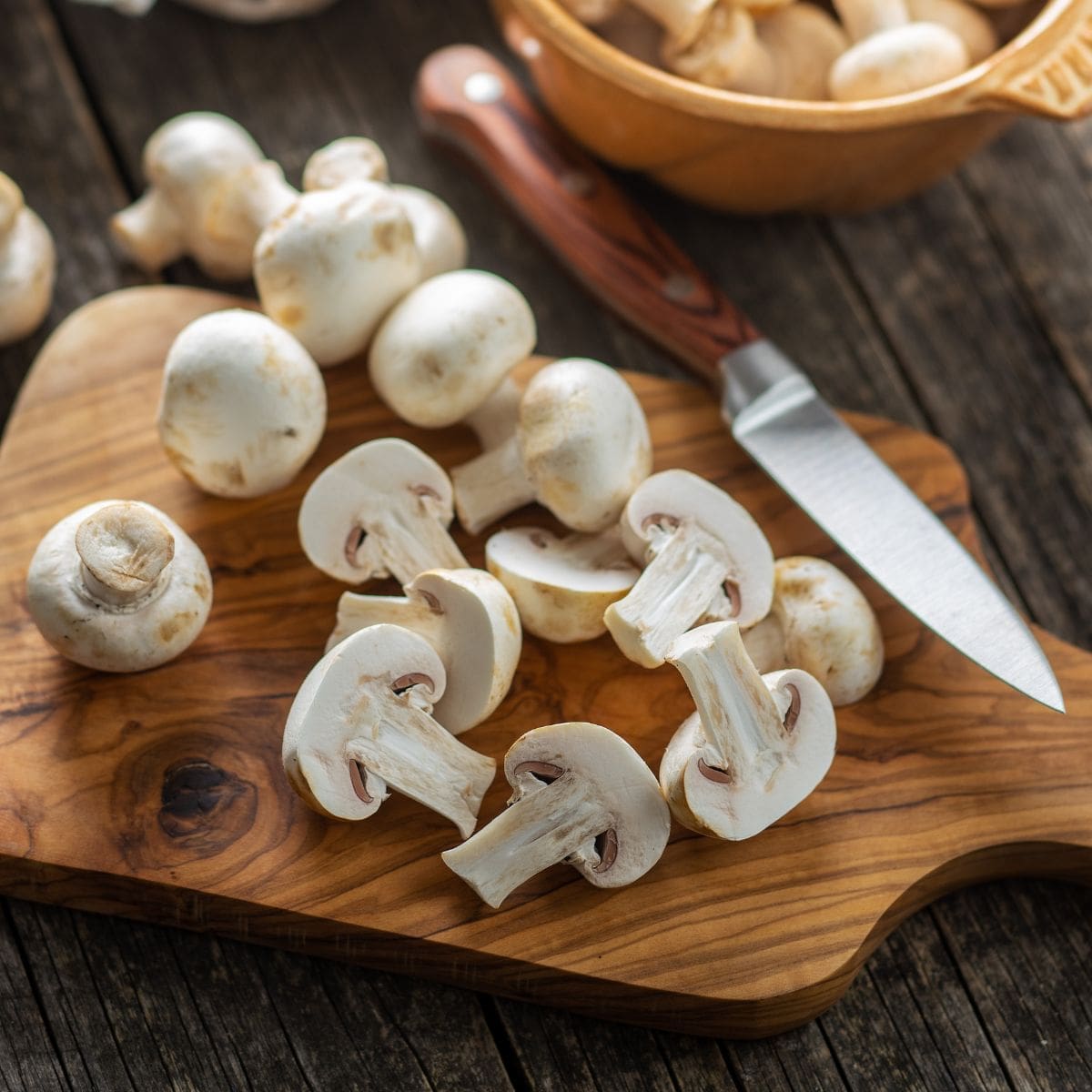 A close-up photo of a variety of sliced mushrooms on a wooden cutting board.