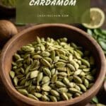 A close-up photo of a wooden bowl filled with cardamom pods on a wooden table.