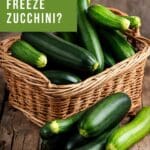 A wicker basket filled with fresh zucchini sits on a wooden table.