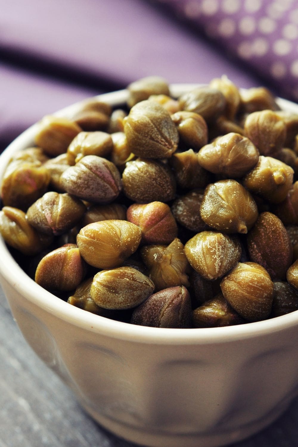 A small, white ceramic bowl filled with green capers. 
