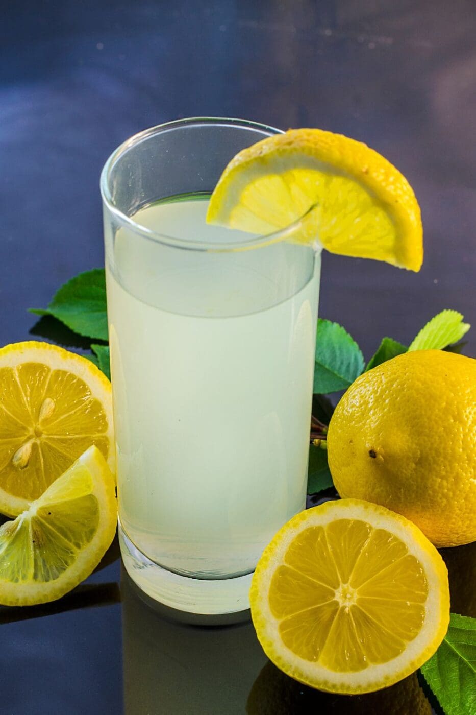 A glass of lemon juice surrounded by sliced lemons on a table.