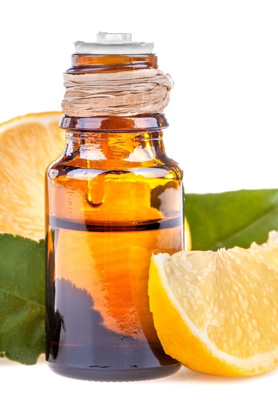 A bottle of lemon oil next to a sliced lemon on a white background.