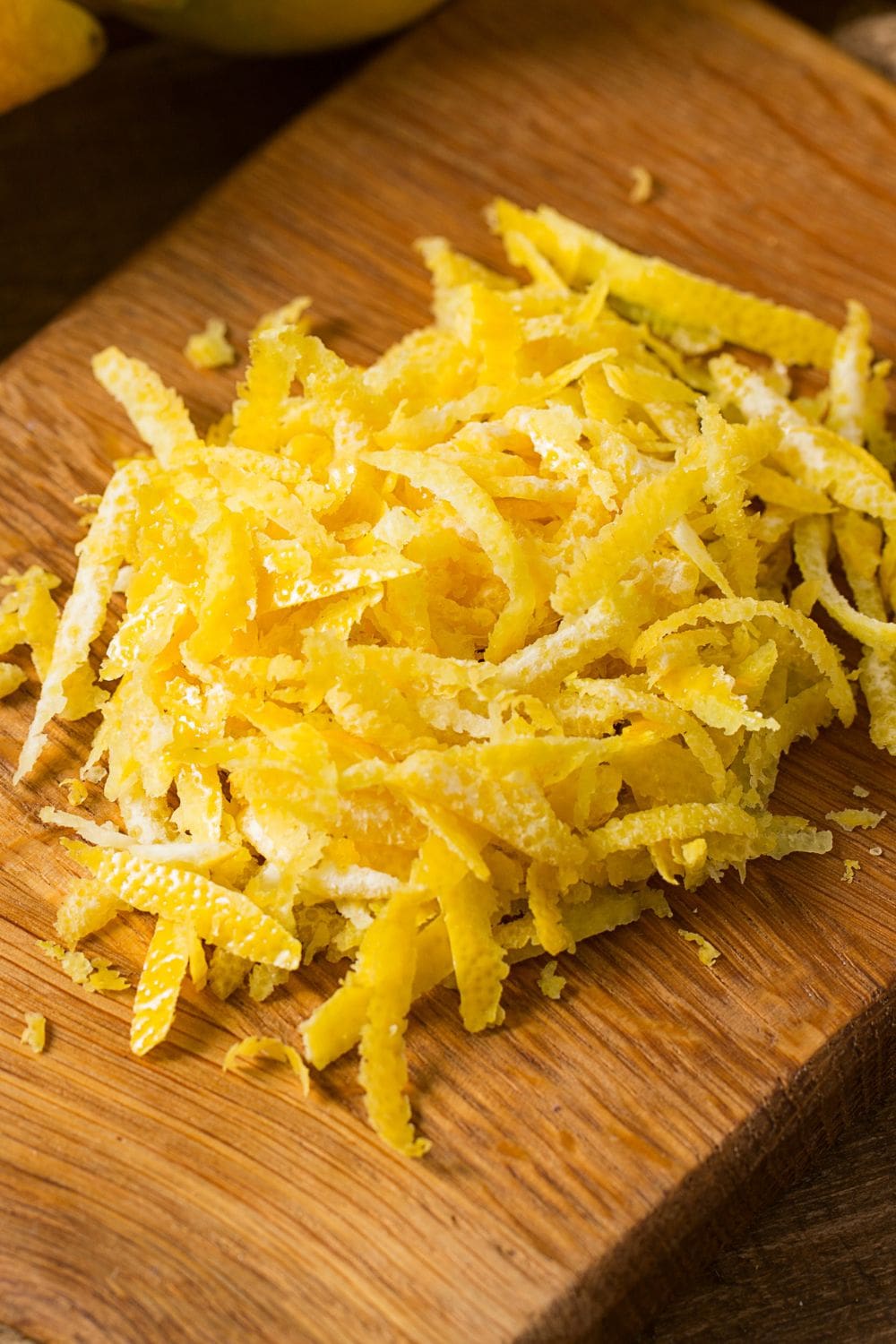 A close-up of a bowl of grated lemon zest on a wooden cutting board.