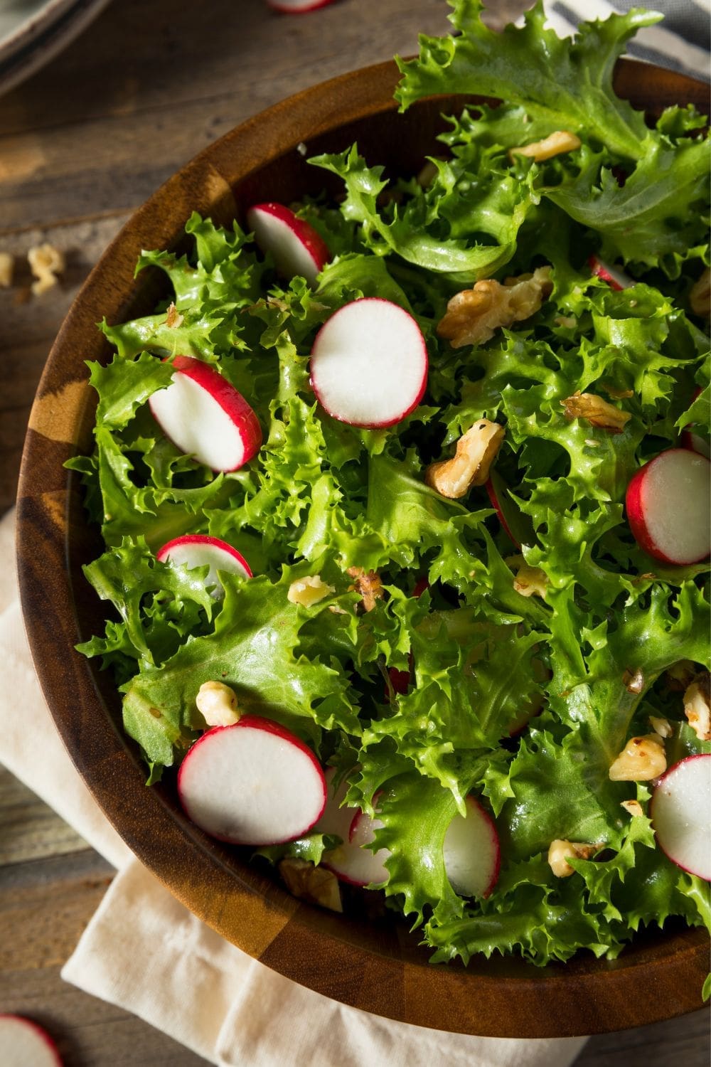 A close-up photo of a rustic wooden bowl filled with a salad made endive and radish.