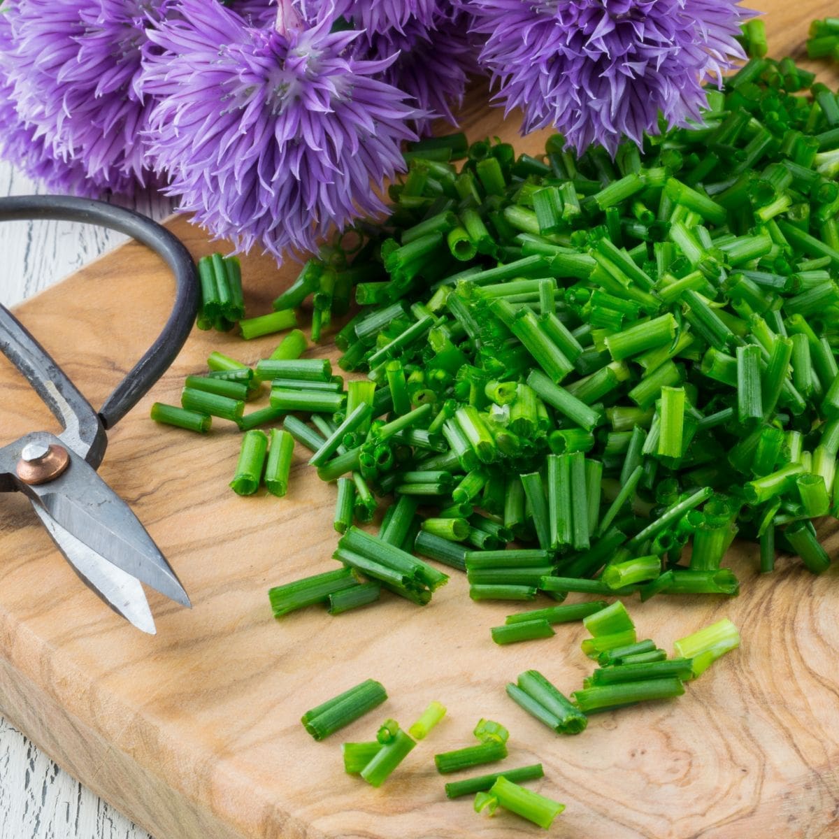 A close-up photo of a wooden cutting board with a pile of freshly chopped chives.