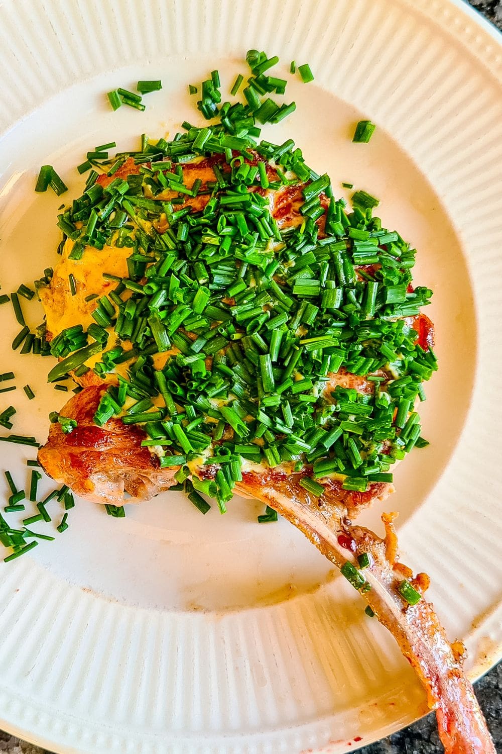A close-up photo of a plate of pork chops topped with chopped chives