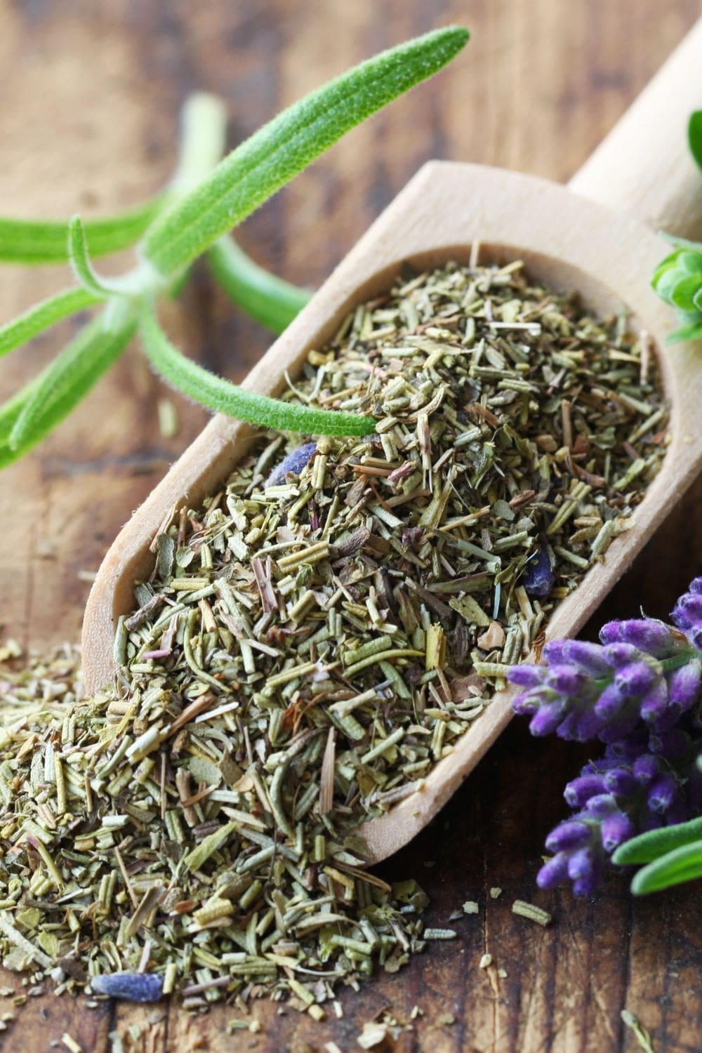 A wooden scoop filled with dried herbs and flowers on a wooden table.