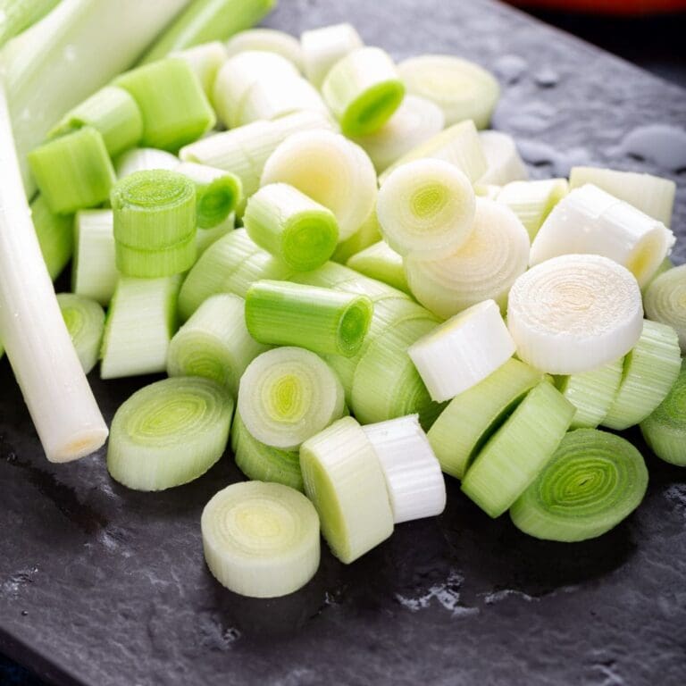 A close-up photo of a pile of chopped leeks on a wooden cutting board.