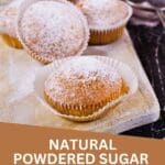 A group of cupcakes dusted with powdered sugar, sitting on a rustic wooden cutting board.