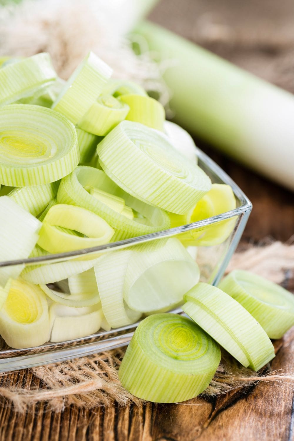 A close-up photo of a bowl of chopped leeks on a wooden table.