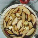 A round ceramic pie dish of baked cinnamon apple slices with the peel on