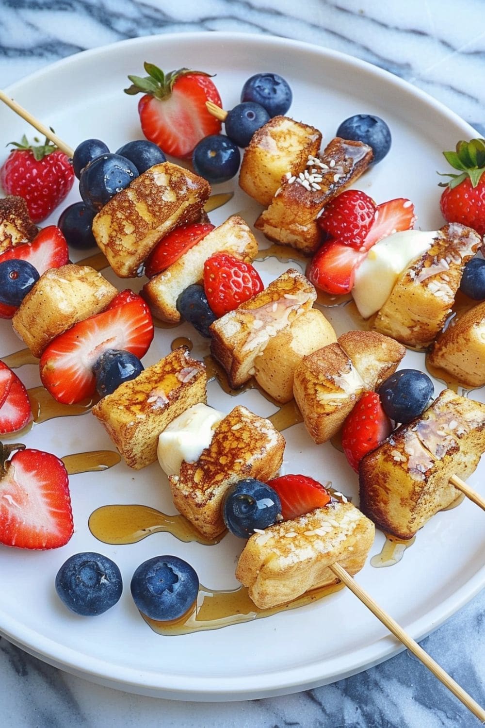 A plate with skewers of French toast bites alternating with strawberries and blueberries.