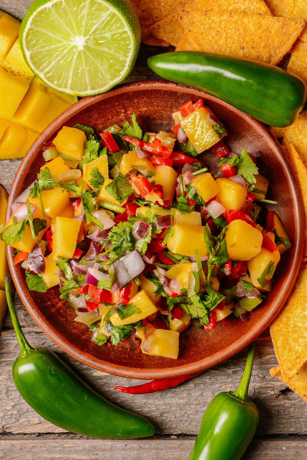 A bowl of mango salsa containing diced mangoes, red onions, jalape&ntilde;os, cilantro, and lime juice, with a side of tortilla chips.