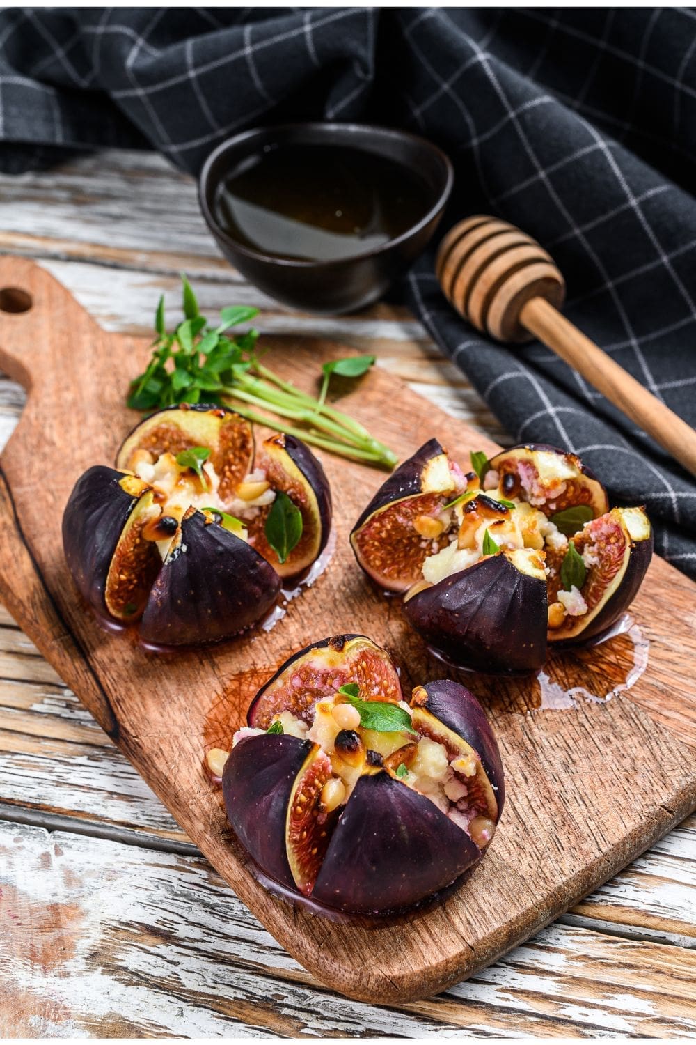 Three roasted figs with honey on a wooden cutting board.