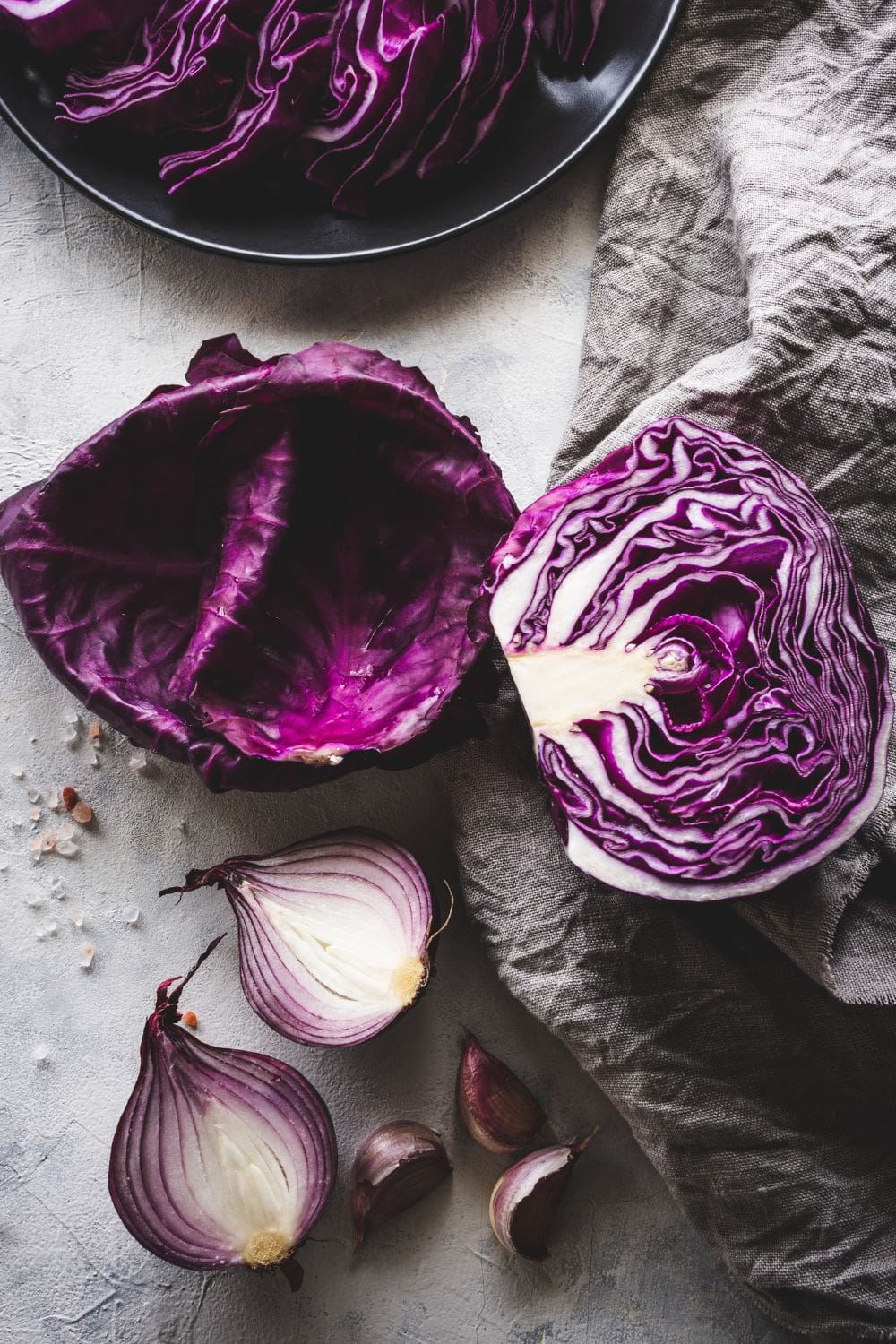 A close-up photo of a red cabbage, onion, and garlic on a rustic wooden table.