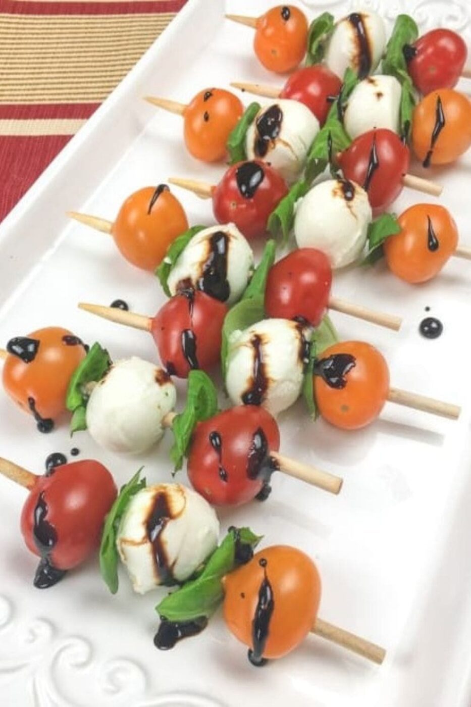 Fresh Caprese skewers with mozzarella, cherry tomatoes, and basil, drizzled with balsamic glaze on a serving platter.