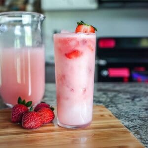 A chilled Pink Drink with ice and sliced strawberries in a mason jar.