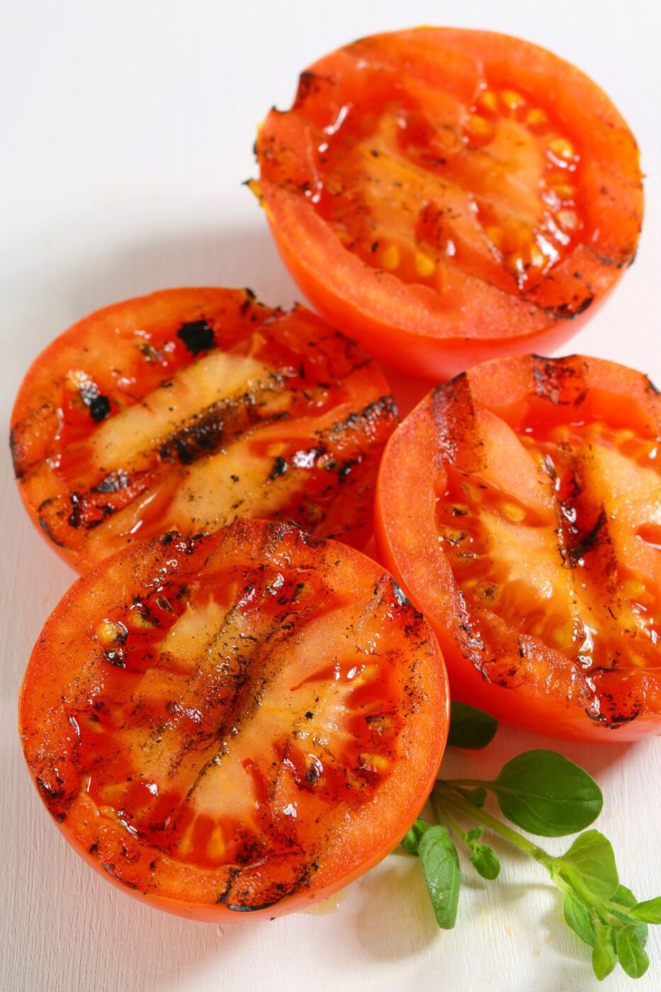 Juicy grilled tomatoes with a slight char, garnished with fresh herbs and olive oil, served on a rustic plate.