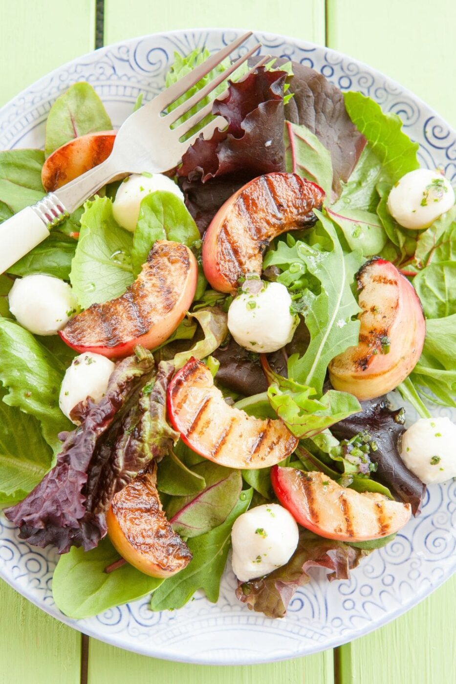 A vibrant summer salad with grilled peaches, greens, and champagne vinaigrette, served on a white plate.