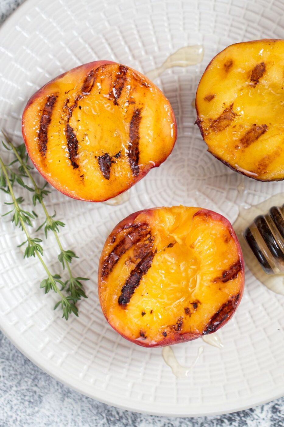 Juicy grilled peaches caramelized with honey, served on a plate with a scoop of vanilla ice cream.