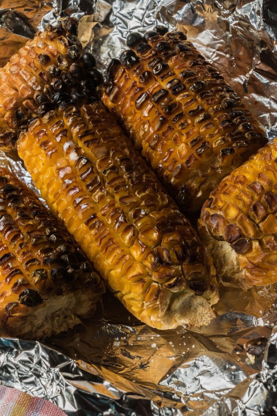 Freshly grilled corn on the cob with a golden char, topped with melted butter on a rustic wooden board.